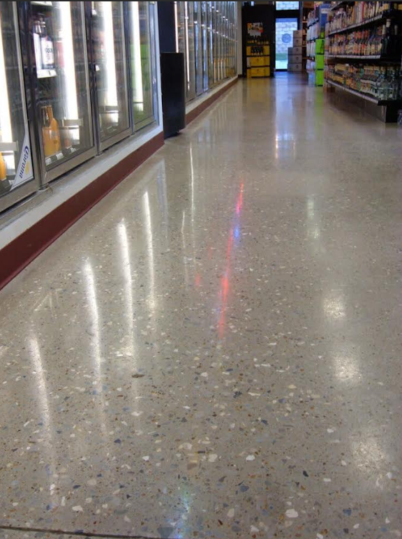 Highly polished aggregate-exposed concrete floor running down a retail store aisle past glass-door coolers