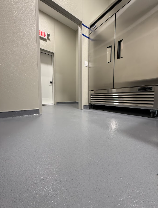 Gray epoxy floor coating by a stainless walk-in cooler in a commercial kitchen