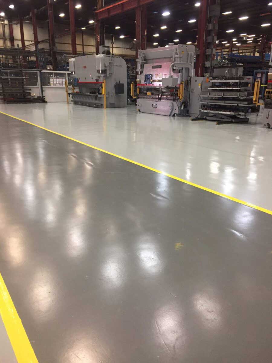 High-gloss gray epoxy floor with bright yellow safety lines in a manufacturing plant with press-brake machinery