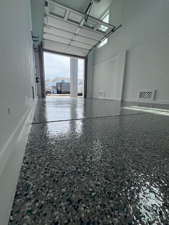Glossy gray, white and black flake epoxy garage floor with the overhead door open to daylight