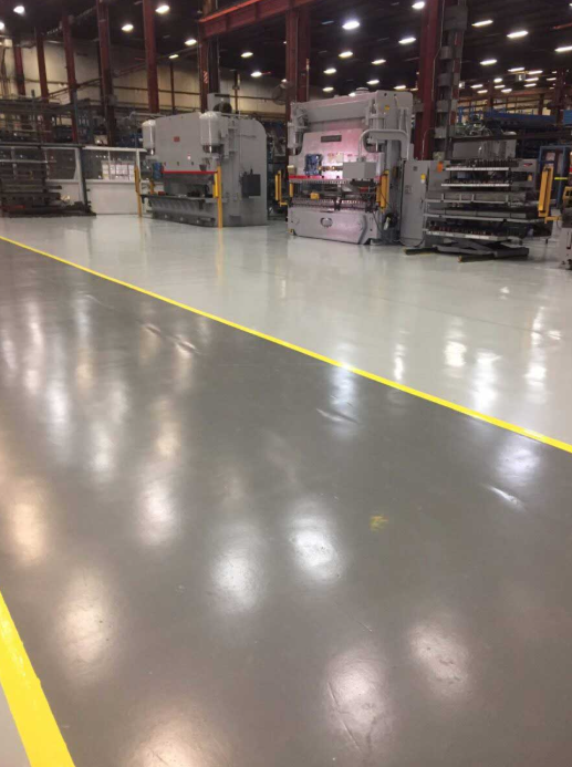 High-gloss gray epoxy floor with bright yellow safety striping in a manufacturing machine shop with press-brake equipment