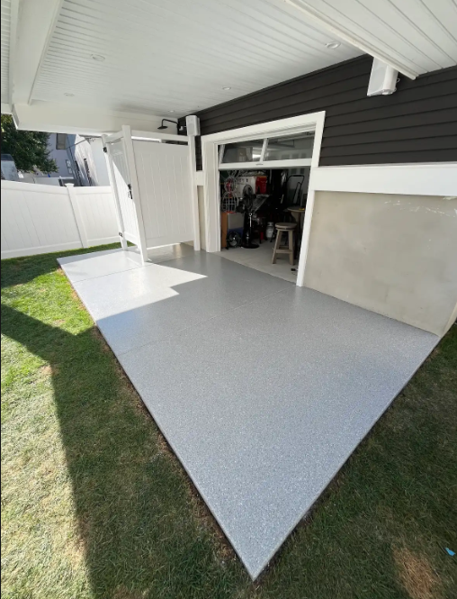 Fresh gray flake epoxy coating on a backyard patio leading into an open garage