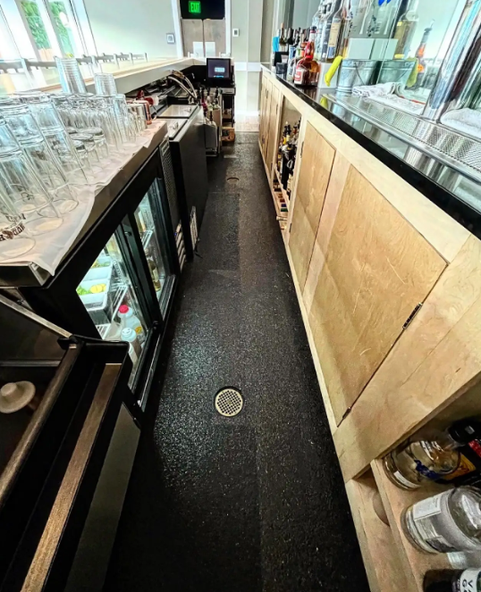 Black flake floor coating behind a commercial bar lined with glassware and bottles