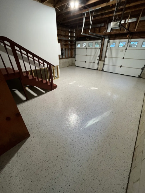 White and gray flake epoxy floor in an unfinished basement with a red wood staircase and white overhead doors