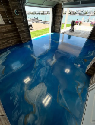 Swirling blue and gold metallic epoxy floor in a boathouse garage opening onto a bay and marina