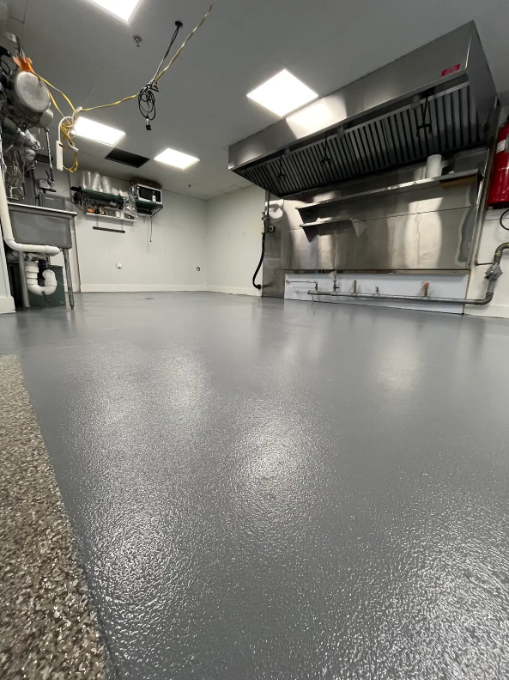 Solid gray epoxy floor in a commercial kitchen with a stainless exhaust hood and prep sinks