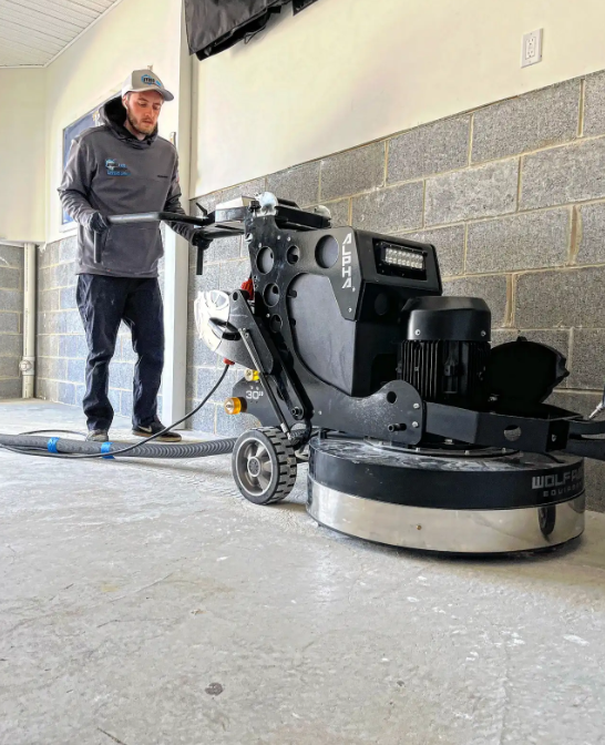 Surface Shield technician grinding a concrete slab with a diamond grinder against a block wall