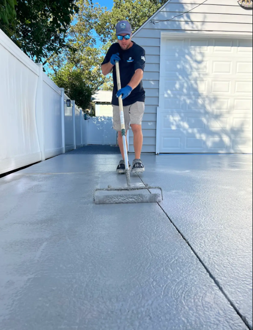 Technician rolling a fresh gray coating across a residential driveway between two homes