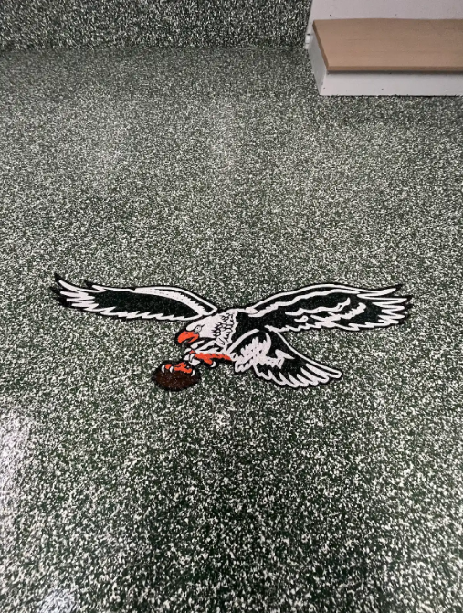 Custom flying-eagle logo inlaid into a green, white, and black flake epoxy garage floor