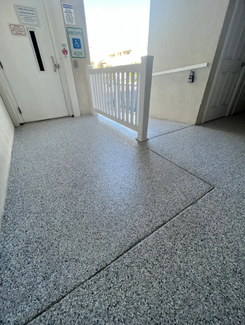 Gray flake coating on an exterior stairway landing with a white vinyl railing