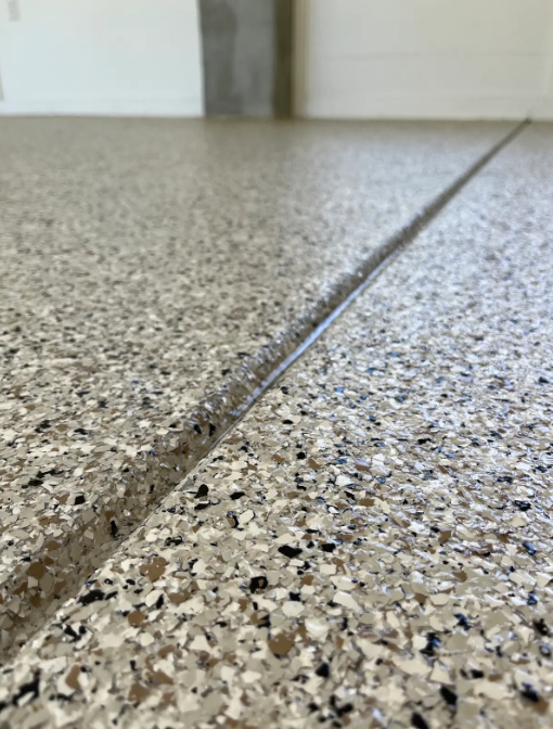 Close-up of a tan, black, and blue flake epoxy floor with a clean metal expansion joint strip