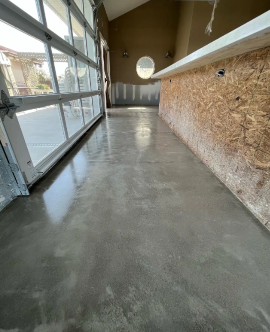Polished concrete floor in a workshop with a glass roll-up door and OSB-sheathed walls