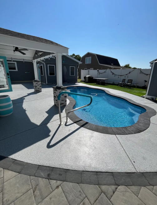 Gray flake concrete coating wrapping a freeform in-ground pool with a paver border in a sunny backyard
