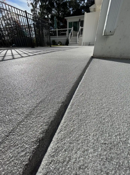 Gray flake concrete coating on an outdoor pool deck beside a black aluminum fence