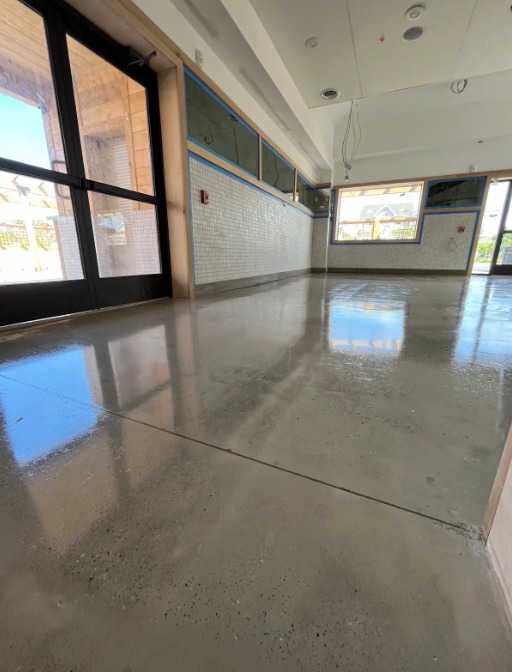 Polished concrete floor in an empty retail storefront with a glass entry door and tiled walls