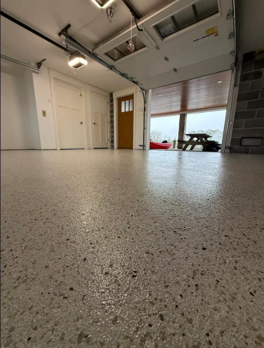 Low-angle view of a tan flake epoxy garage floor with the overhead door open to a waterfront
