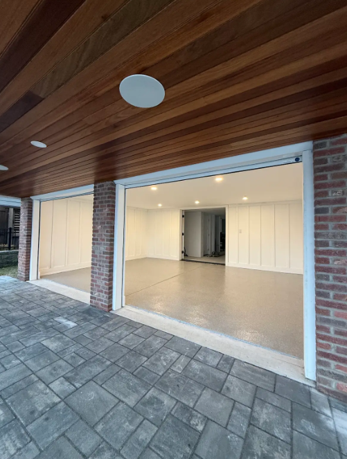 Tan flake epoxy floor in an open room beneath a cedar-ceilinged carport with brick columns and a paver patio