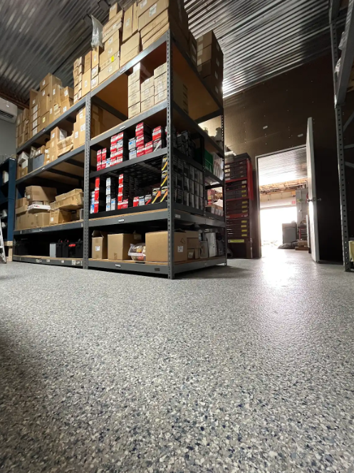 Durable gray flake floor coating in an industrial warehouse stockroom with steel shelving